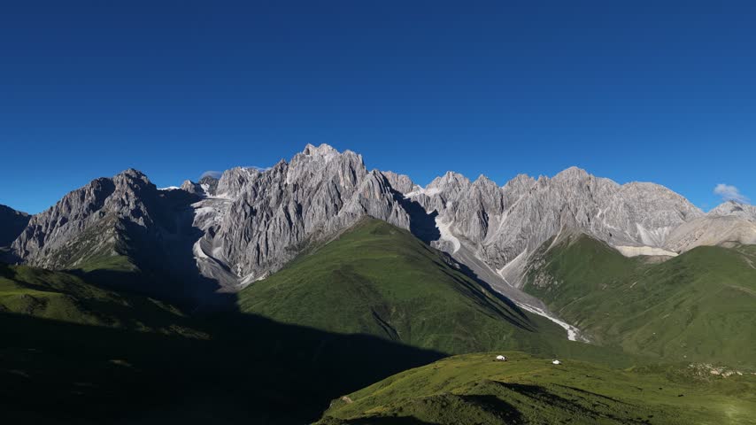 Landscape of green grassland in high altitude mountain top, with snowcapped mountains in the distance	