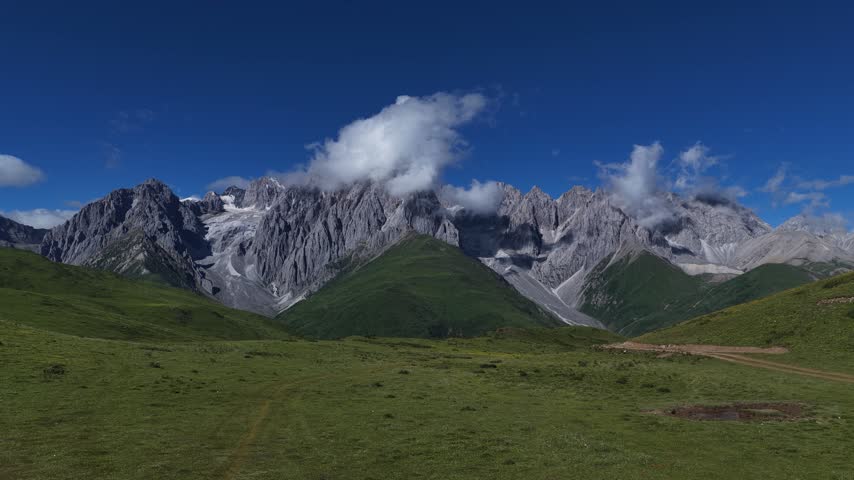 Landscape of green grassland in high altitude mountain top, with snowcapped mountains in the distance	