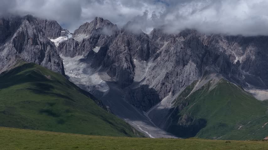 Landscape of green grassland and beautiful lake in high altitude mountain top, with snowcapped mountains in the distance	