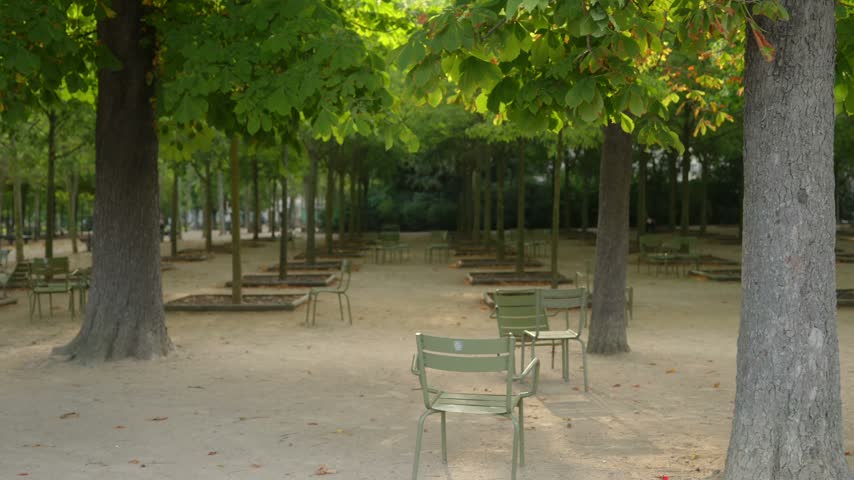Rows of empty green metal chairs beneath mature leafy trees along a shaded gravel path in Luxembourg Gardens, Paris, France