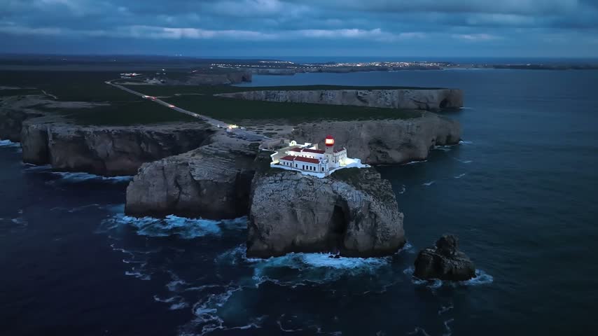Drone view of the Lighthouse of Cabo de Sao Vicente in Sagres, Algarve, Portugal, at night with cliff fortress and Atlantic Ocean. Orbit parallax shot