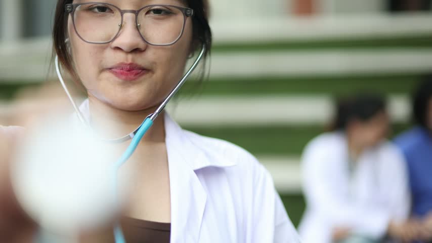 Smiling female medical student holds stethoscope and looks camera before class  modern university embodying academic determination education and fresh start classmates visible in the background.