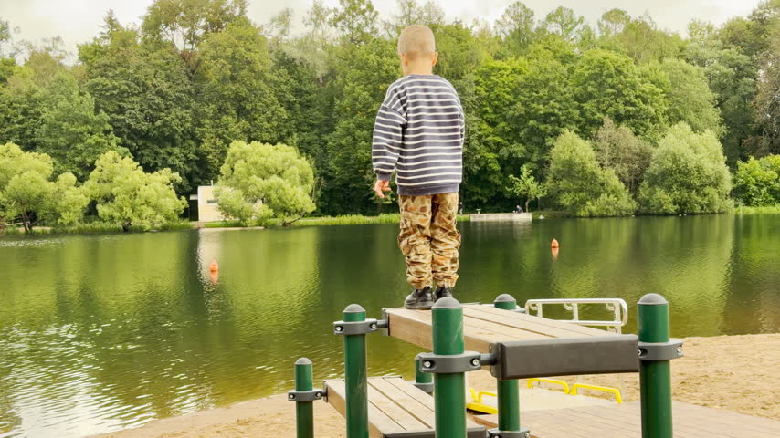 A playful young boy jumps on a wooden dock. He feels joyful and excited during his outdoor adventure at Kolonistsky Pond Beach in Pushkin, Saint Petersburg.