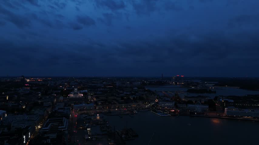 Wide aerial panorama of Helsinki at nightfall with glowing landmarks historic rooftops waterfront buildings and illuminated streets under a darkening sky
