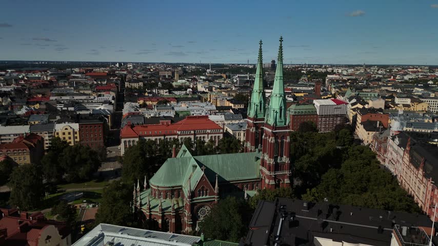 Aerial drone view of St Johns Church in Helsinki surrounded by historic city buildings green parks and urban streets under soft daylight