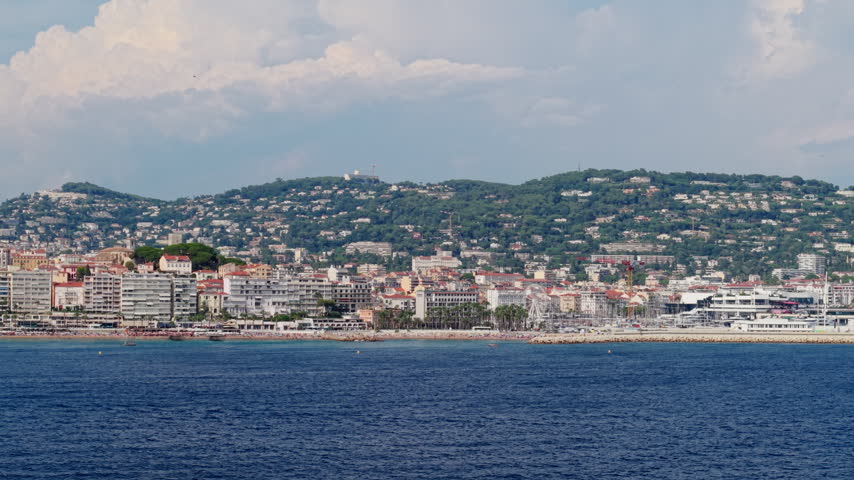 Drone moves from right to left along Cannes, showing the waterfront city and densely built residential hills behind.