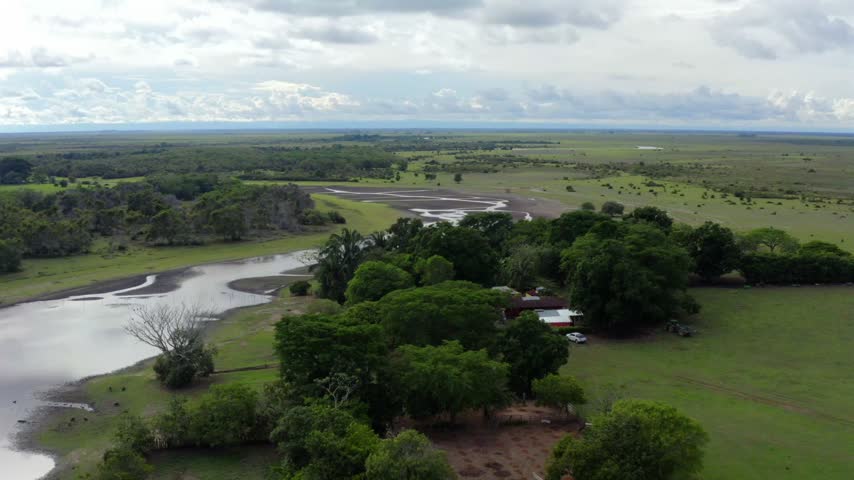 Winding river cutting through green savanna grassland scattered trees and small ponds in the Llanos Orientales region of Colombia, aerial pullback