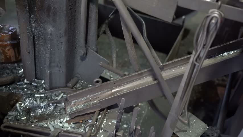 Worker using tongs to pull a glowing forged bolt head from the press die