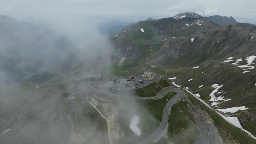 Mist drifts across the Edelweissspitze summit parking area and winding Grossglockner high alpine road as the camera flies above.