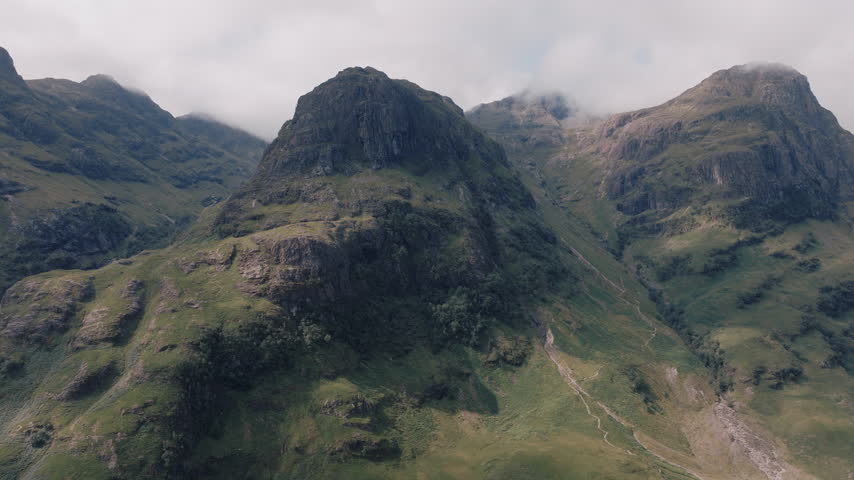Aerial close up of the Three Sisters of Glencoe, mist clinging to the summits above a winding road.