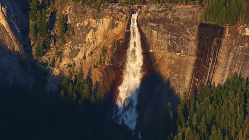 Granite cliffs and Nevada Fall in Yosemite Valley caught in golden sunset light from Glacier Point viewpoint California