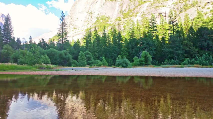 Granite peaks, blue sky, and surrounding pine forest reflected in the crystal clear waters of Mirror Lake in Yosemite National Park, California.
