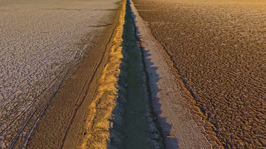 An earthen ridge cuts across the white mineral crust and golden evaporite beds of Bonneville Salt Flats Utah