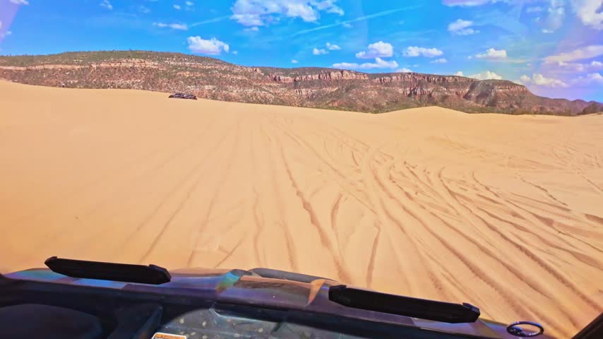 An ATV powers across rippling reddish orange dunes illuminated by evening sunlight at Coral Pink Sand Dunes State Park Utah