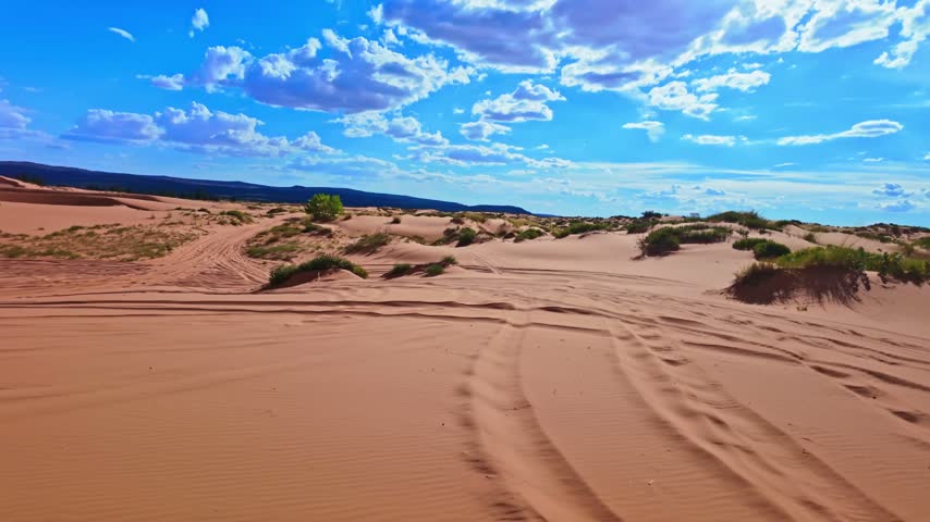 An ATV powers across rippling reddish orange dunes illuminated by evening sunlight at Coral Pink Sand Dunes State Park Utah