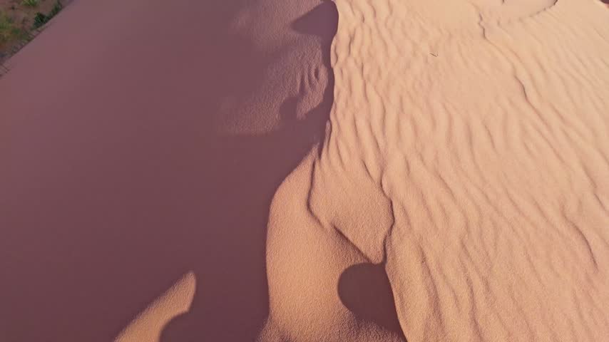 Golden sunset light bathes sweeping reddish sand ridges and desert terrain from atop a massive dune in Coral Pink Sand Dunes State Park