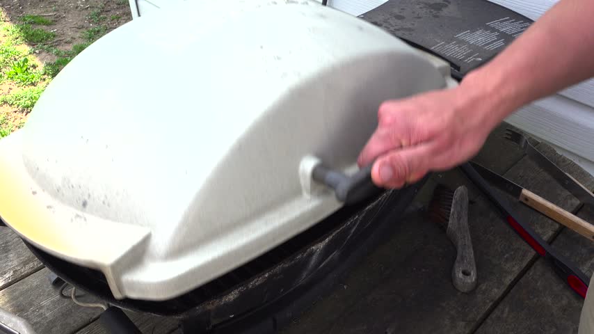 A barbecue lid is opened to reveal beef steaks sizzling on hot grill grates, pushing in close before the lid is closed by a person again.