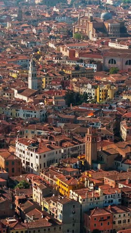 Slow cinematic drone flight moving over dense terracotta rooftops and historic bell towers in Venice Italy during golden hour sunlight providing panoramic cityscape views.