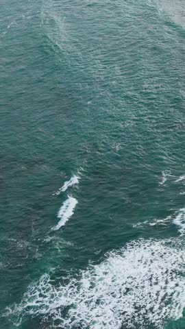 Aerial top down shot of turquoise ocean waves breaking against a rocky coastline in Australia.