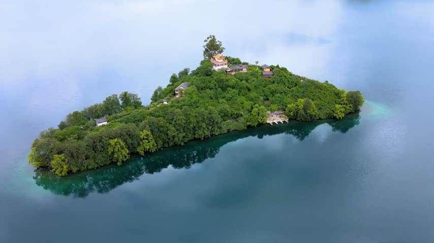 Aerial view of the lake center island in Lugu Lake Yunnan China. The island is covered with dense forests, with buildings dotted on it, and the lake water is as smooth as a mirror, showing the quiet scenery of the plateau lake.