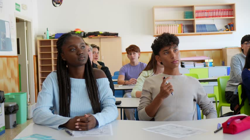 Attentive multiethnic high school students sitting at their desks, actively participating and engaging in a classroom lesson, while listening to the teacher and answering questions