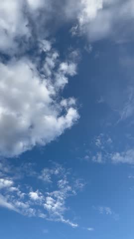 A static vertical shot of dramatic white and gray clouds drifting across a deep blue sky on a partly cloudy day.