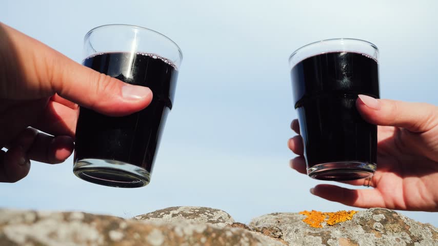 Two hands clinking glasses of homemade red wine outdoors against the sky, winery tour and tasting concept. High quality 4k footage