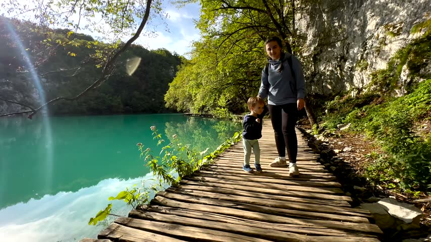 Family follows a wooden path beside a turquoise lake in a lush protected forest.