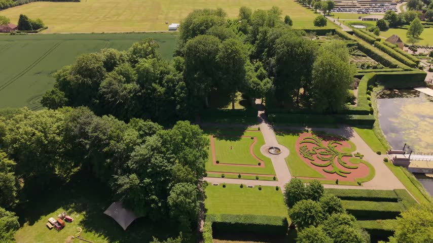 A smooth aerial lateral movement reveals Egeskov Castle alongside its iconic geometric gardens, manicured hedges, and beautifully designed Renaissance landscape.