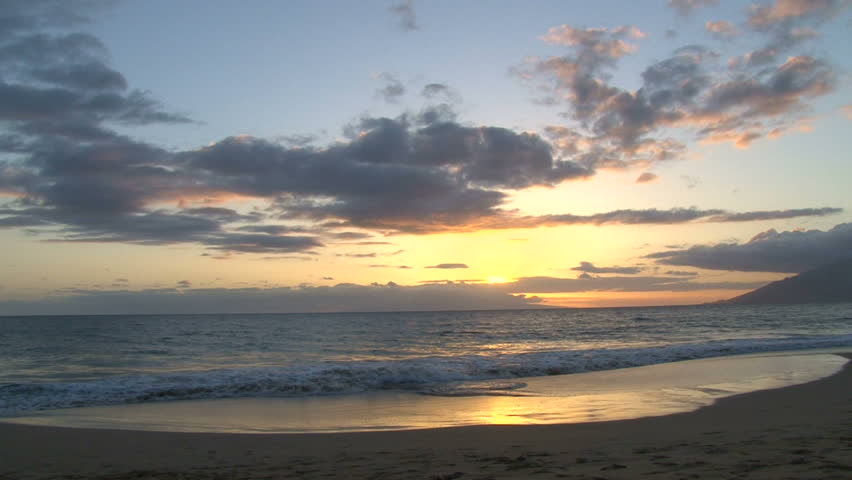 Camera panning shot over Pacific Ocean from sandy beach in Hawaii.