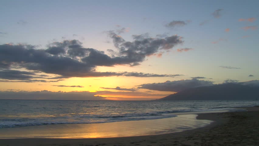 Sunset over Pacific Ocean from sandy beach in Hawaii.