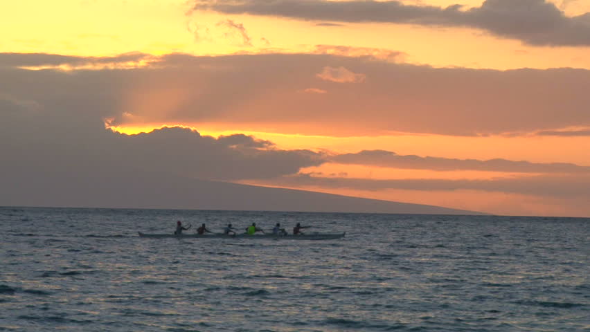 Rowing team racing on ocean at sunset.