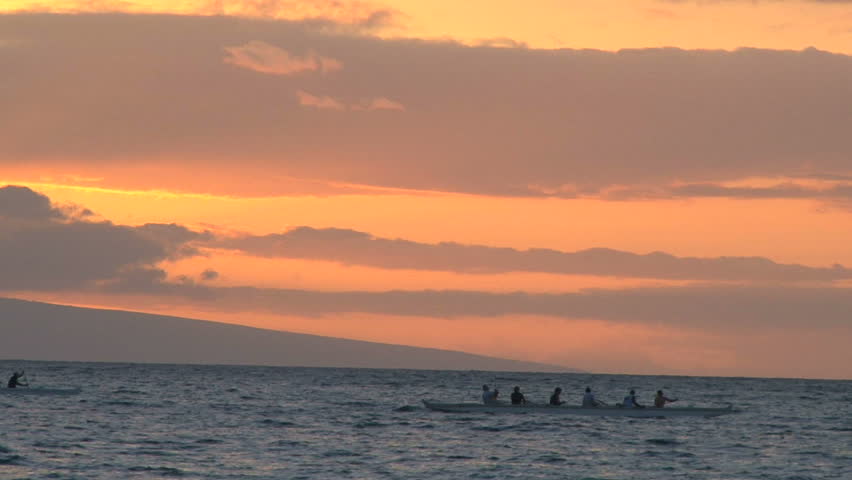 Rowing teams racing on ocean at sunset.