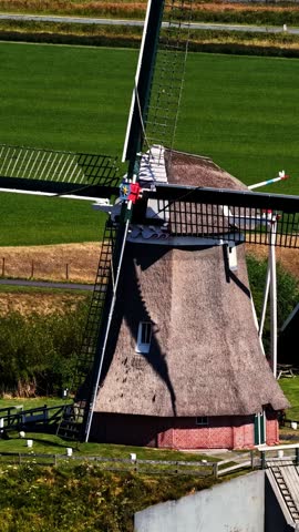 Traditional thatched Dutch windmill stands beside storage tanks and cranes at Eemshaven energy port in Groningen, Netherlands, contrasting old and new