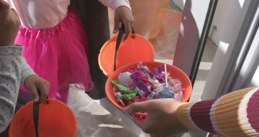 African American child girls with pumpkins reaching for tray as adult offering candy, copy space. Doorway, porch, threshold, halloween, exchange, sweets, costume