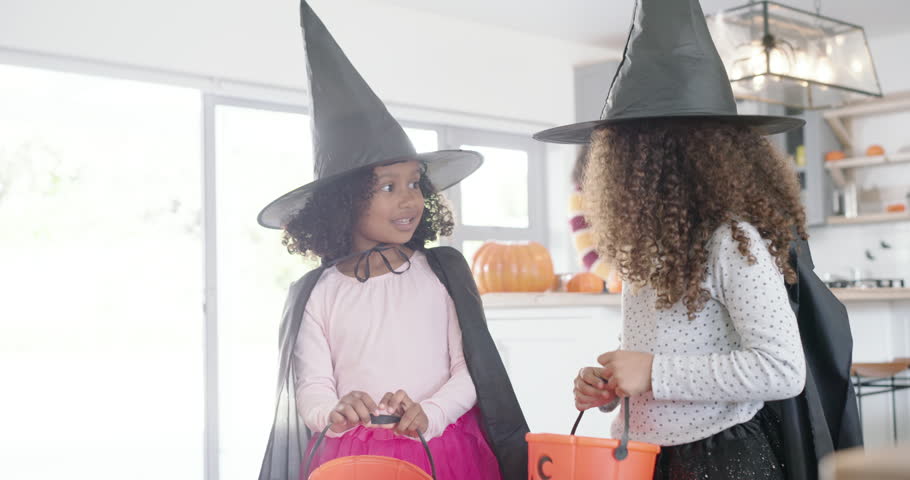 African American female children in witch hats checking buckets while mom carving pumpkin. Halloween, jackolantern, costumes, kitchen, daylight, openplan, family