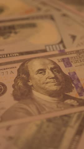Close-up of 100 dollar bills arranged on table in portrait format with Benjamin Franklin portrait highlighted under dimmed warm light