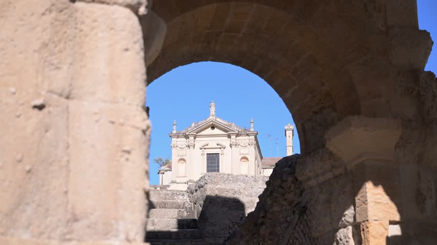 Baroque facade of Basilica di Santa Maria Maggiore appears through a rough stone arch and steps under clear daylight sky.