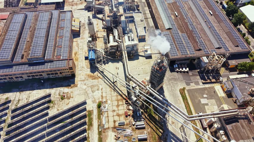 Buildings with solar panels on the roof and large pipes connected to various structures. It is a clear day with some steam rising from one area.
