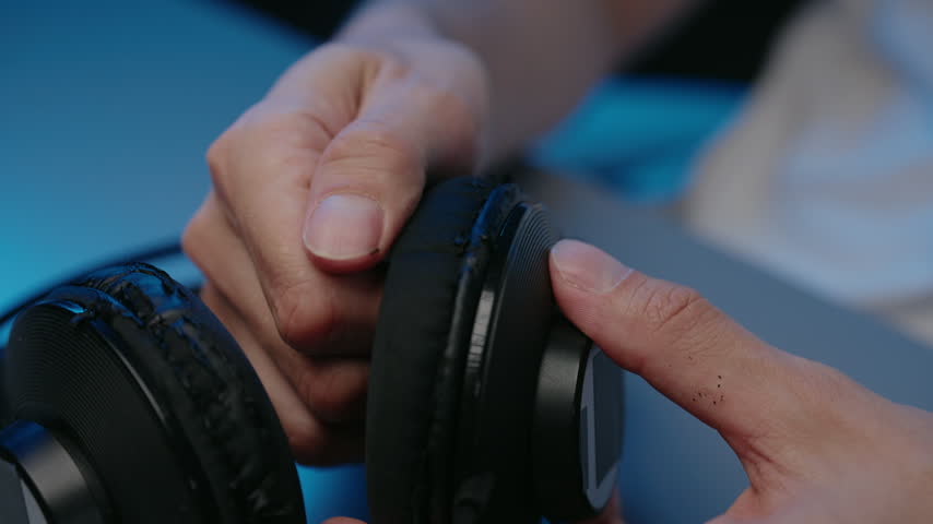Closeup cropped shot of hands peeling off old, worn, flaking faux leather from headphone ear pads. Concept of DIY repair, maintenance, product obsolescence, upcycling electronic devices.