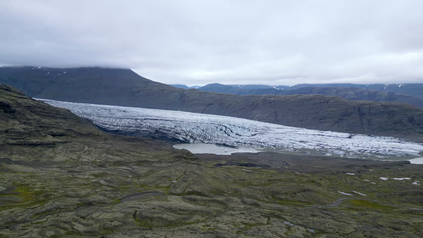 A majestic Skálafellsjökull glacier stretches across a rugged Icelandic mountain valley under a cloudy sky, creating a serene and epic natural atmosphere.