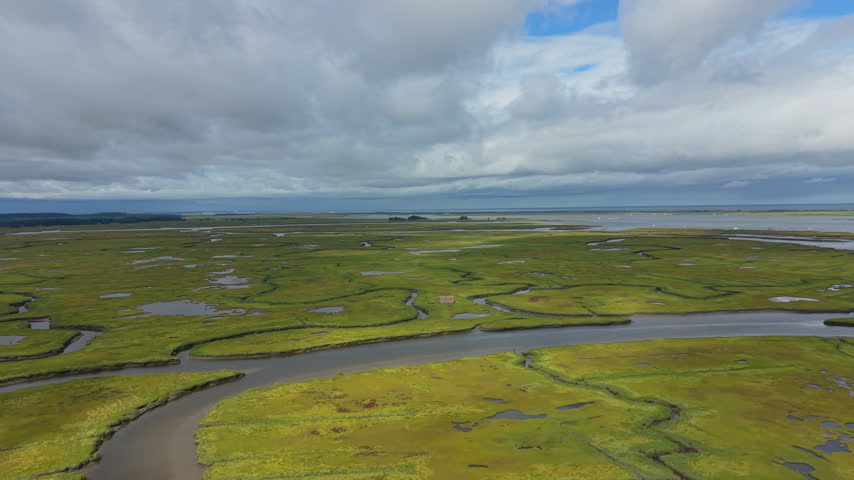 Aerial forward flight over the Ipswich salt marsh toward the Atlantic under dramatic storm clouds, epic view in Massachusetts