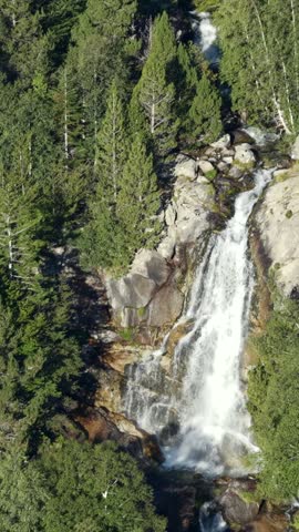 Aerial view of Cascada de Molieres waterfall cascading through alpine forest and granite mountain peaks, Val d