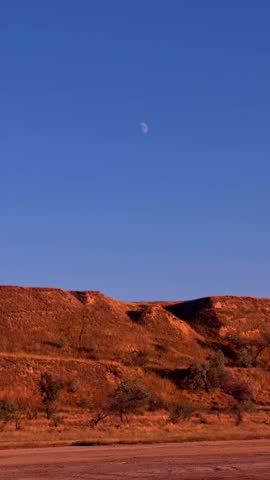 Red Clay Cliffs and Daytime Moon in Clear Blue Sky