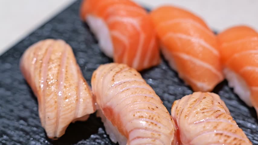 Fresh salmon nigiri sushi presented in both lightly torched and unseared styles, showcasing contrasting textures, colors and flavors in Japanese cuisine.