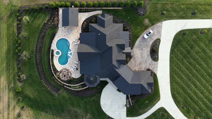 Directly above a luxury home with a curved swimming pool, stamped patio and manicured lawn on a large lot in Forest, Virginia. Aerial top down shot