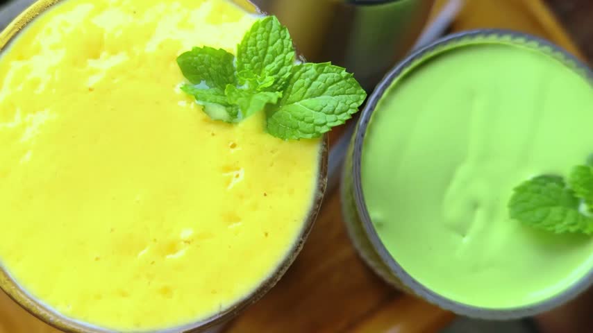 Creamy organic matcha green tea latte and mango smoothie in tall glasses.