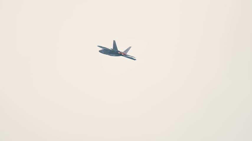 An F-22 Raptor Stealth Fighter Deploys Countermeasure Flares While Banking in Overcast Skies.
