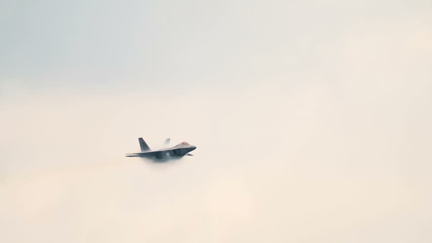 An F-22 Raptor Stealth Fighter Flies Profile Against a Bright Sky With Vapor Condensation Below Its Fuselage.