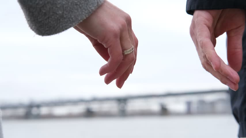 Close up of couple reaching hands toward each other with wedding rings by river